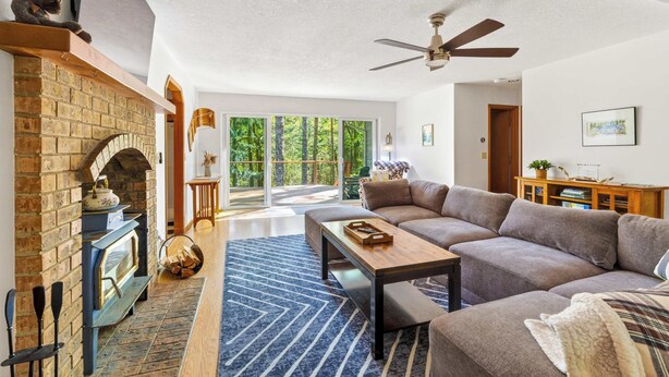 A spacious living room with a fireplace, a sofa, a coffee table, and a ceiling fan. - Relaxing River Lodge • Hot Tub • Family Friendly (Rhododendron)