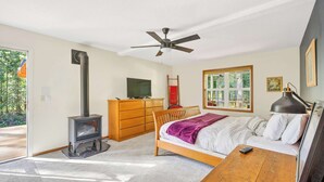 A bedroom with a bed, a wooden dresser, a TV, a ceiling fan, and a fireplace. - Relaxing River Lodge • Hot Tub • Family Friendly (Rhododendron)
