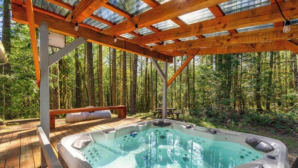 A hot tub under a wooden pergola in a forested area. - Relaxing River Lodge • Hot Tub • Family Friendly (Rhododendron)