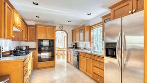 A spacious kitchen with wooden cabinets, stainless steel appliances, and a tiled floor. - Relaxing River Lodge • Hot Tub • Family Friendly (Rhododendron)