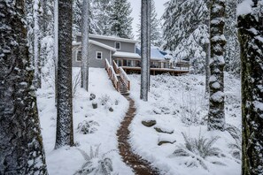 A snow-covered pathway leading to a house with a deck, surrounded by trees. - Winter Lodge • Hot Tub • Wood Stove • Sleeps 10 (Rhododendron)