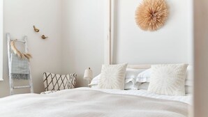 Una cama bien hecha con sábanas blancas y almohadas estampadas, una mesita de noche con una lámpara y un adorno en la pared.