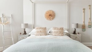 Un dormitorio con cama, dos mesitas de noche, una lámpara de pared, un adorno en la pared y una escalera de madera.