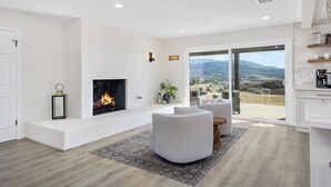 A modern living room with a fireplace, white sofas, and a view of the countryside through large sliding doors.