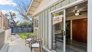 Una veranda riparata con tavolo e sedie, una porta scorrevole in vetro che dà su un ambiente interno, e un recinto in legno sullo sfondo.