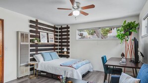 Una stanza compatta con un letto, una scrivania, una sedia, una ventola a soffitto e una finestra.