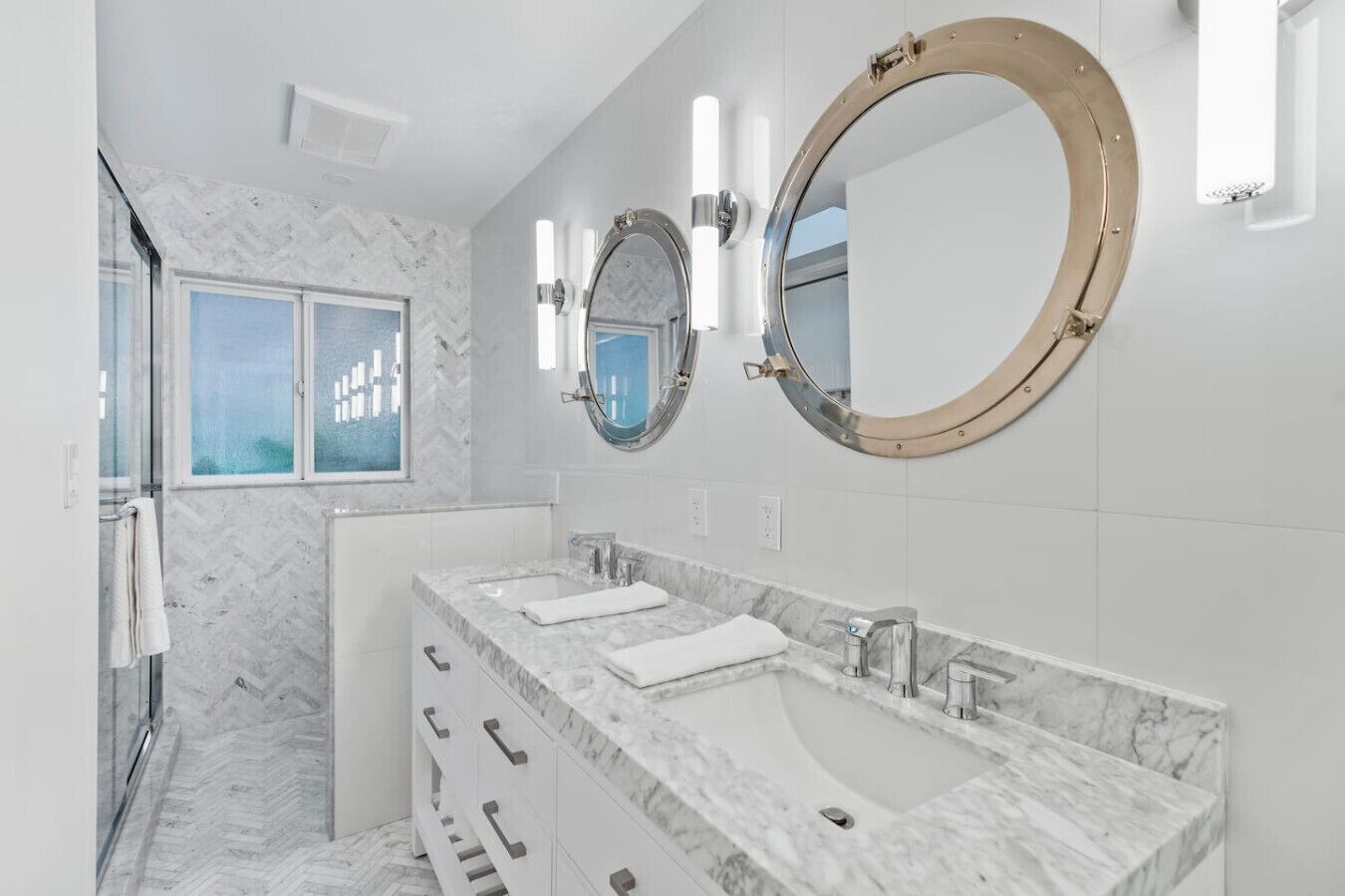 A modern bathroom with two sinks, marble countertops, and large wall mirrors.