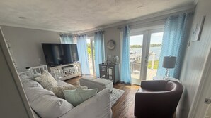 A living room with a sofa, a television, and a view of the outdoors. - Amazing Water Front 4-bedroom estate in charming Narragansett with AC, WiFi (Narragansett)