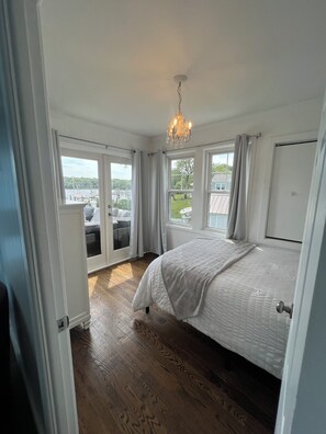Une chambre à coucher avec un grand lit, un lustre et une vue sur un quai et la verdure environnante.