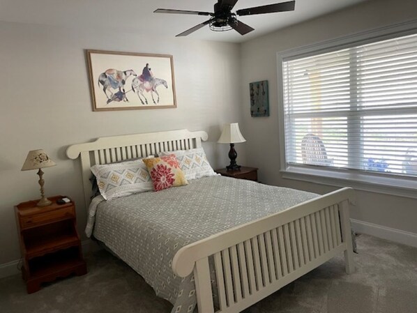 Une chambre à coucher avec un lit, un ventilateur de plafond, une fenêtre avec des stores et des œuvres d’art accrochées au mur.