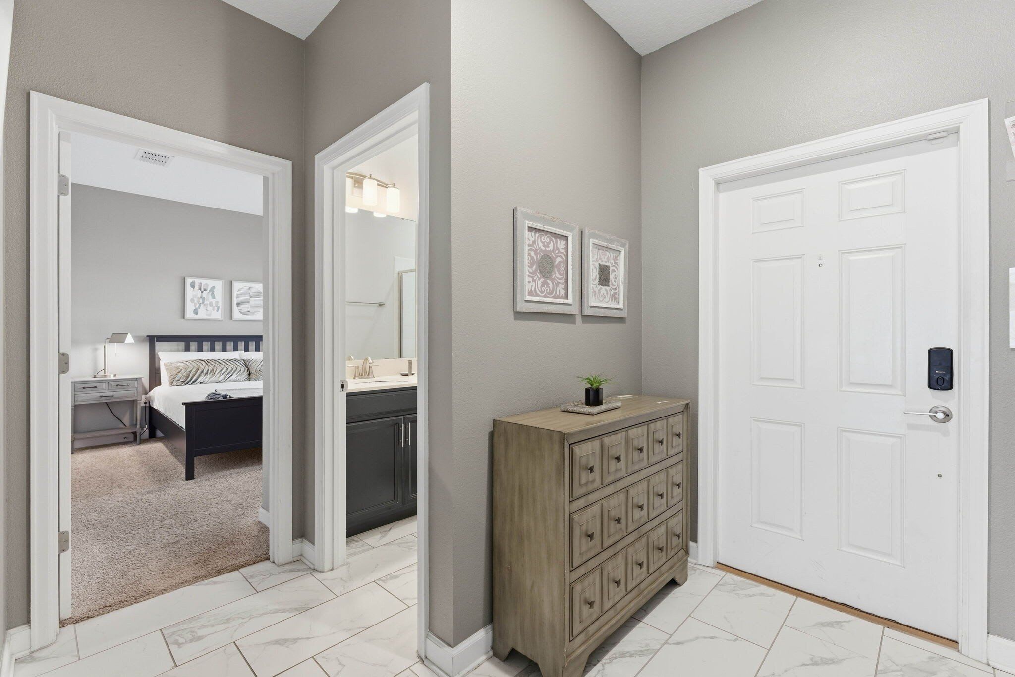 Un couloir avec une commode en bois, une porte blanche et des œuvres d’art encadrées accrochées au mur.