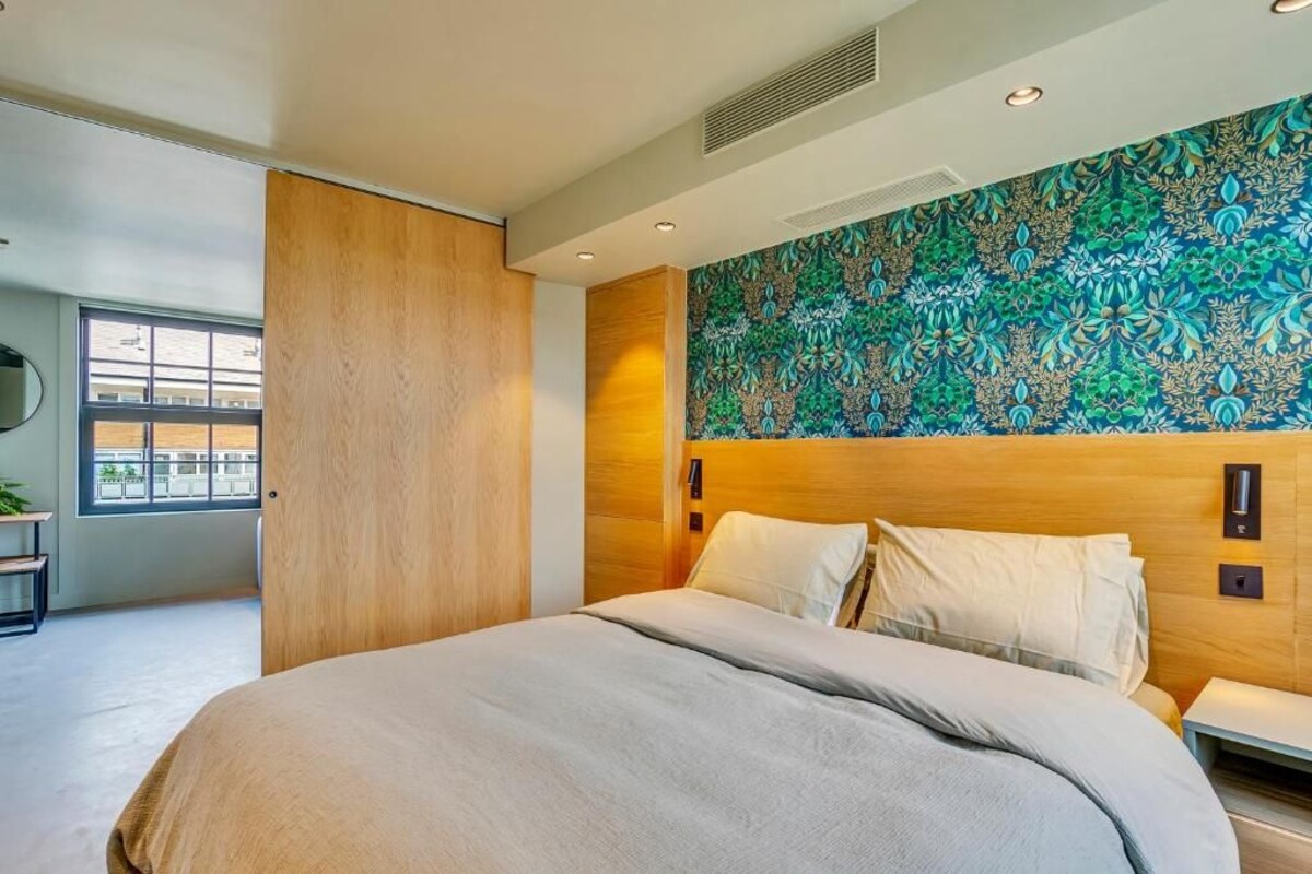 Ein modernes Hotelzimmer mit einem großen Bett, einem Holzkopfende, einer Wand mit Muster und einem Fenster mit Blick.