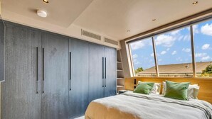Une chambre dotée d’une grande armoire, d’un lit avec des oreillers verts et offrant une vue sur l’extérieur grâce à une grande fenêtre.
