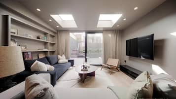 A modern living room with a sofa, coffee table, and TV. There is a bookshelf and a painting on the wall.