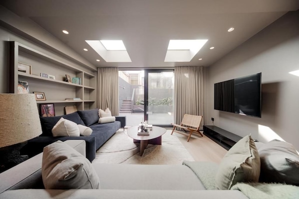 A modern living room with a sofa, coffee table, and TV. There is a bookshelf and a painting on the wall. - Kings House (London)