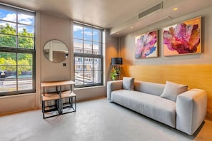 A modern living room with a grey sofa, a round mirror, a small table, and artwork on the wall. - Kings House (London)