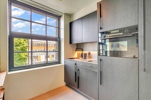 Eine moderne Küche mit grauen Schränken, einem eingebauten Ofen und einem Fenster mit Blick auf Gebäude und Bäume.