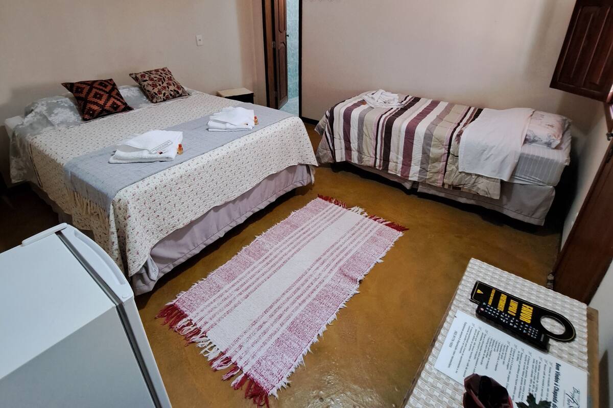 Una habitación pequeña y acogedora con dos camas, un refrigerador, un tapete y una bicicleta en el suelo.