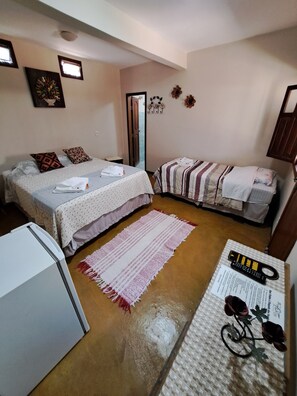 A small, cozy room with two beds, a refrigerator, a rug, and a bicycle on the floor. - POUSADA BEIJA-FLOR (Alto Paraiso de Goias)