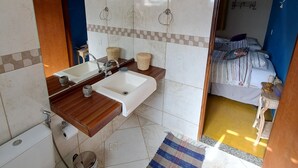 A bathroom with a toilet, sink, and mirror. There is a blue door leading to a bedroom with a bed and a small table.