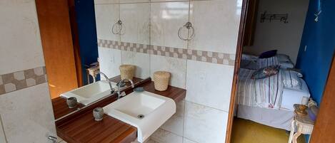 A bathroom with a toilet, sink, and mirror. There is a blue door leading to a bedroom with a bed and a small table.