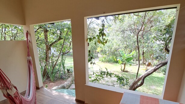 A room with a hammock, a chessboard, and large windows overlooking a garden.