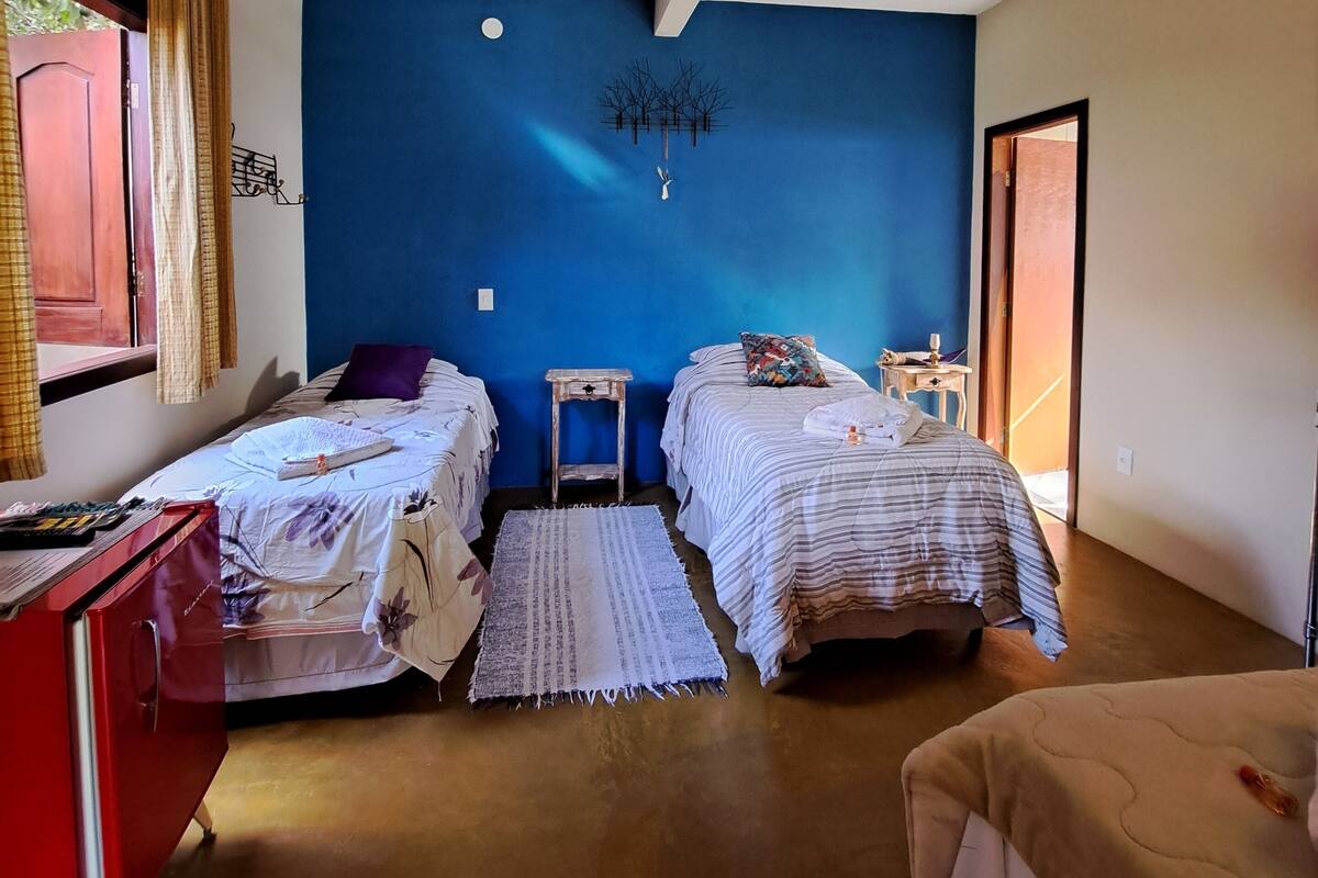 Una habitación con dos camas, un aparador rojo, una mesita y una pared azul decorativa.