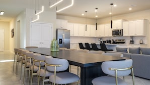 Une cuisine moderne avec des meubles blancs, des appareils en acier inoxydable et un îlot central doté de tabourets de bar.