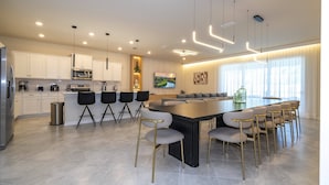 Une cuisine moderne avec des meubles blancs, un îlot central doté de tabourets de bar et un coin repas avec une grande table.