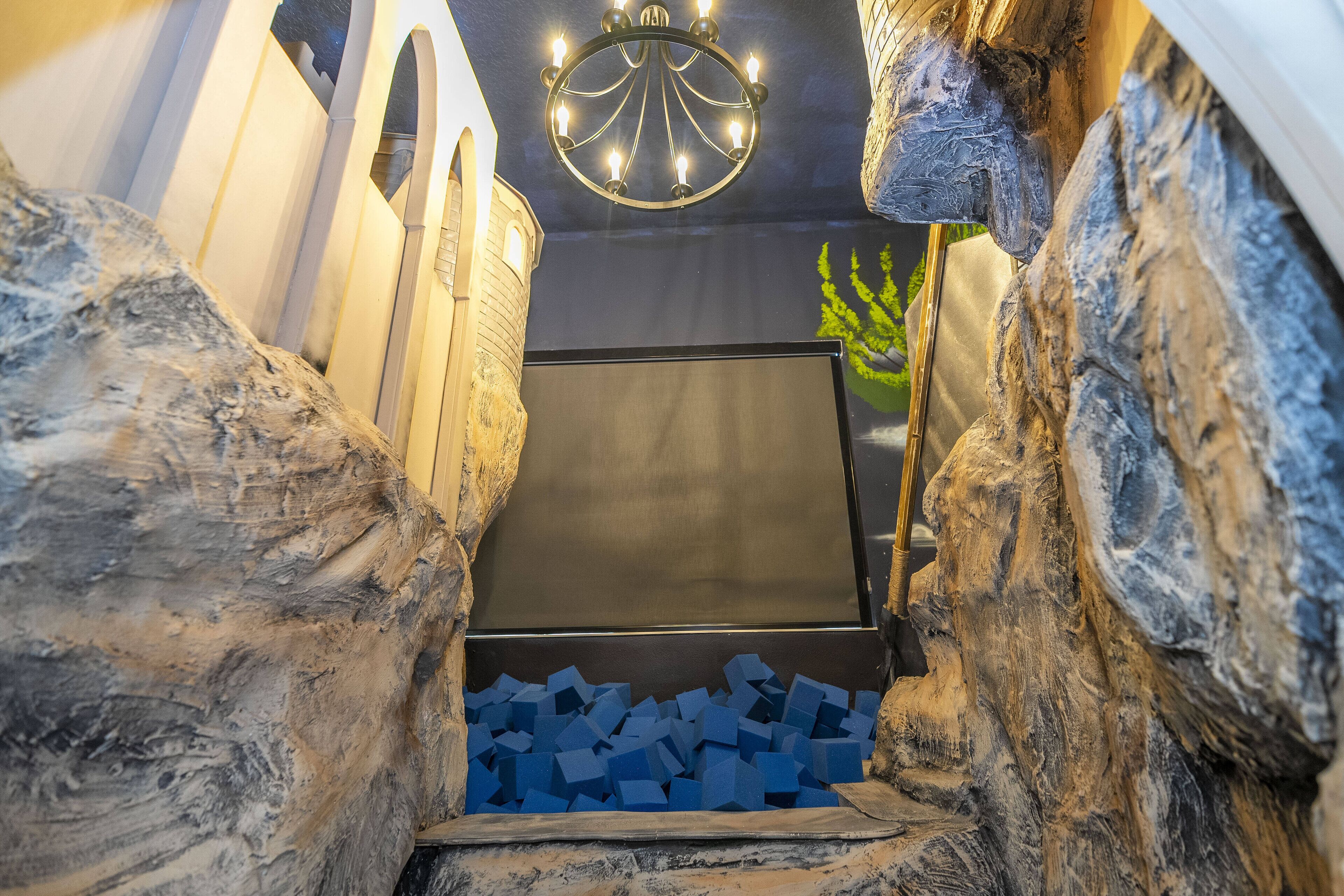 A room with a large screen, stone walls, and a chandelier.