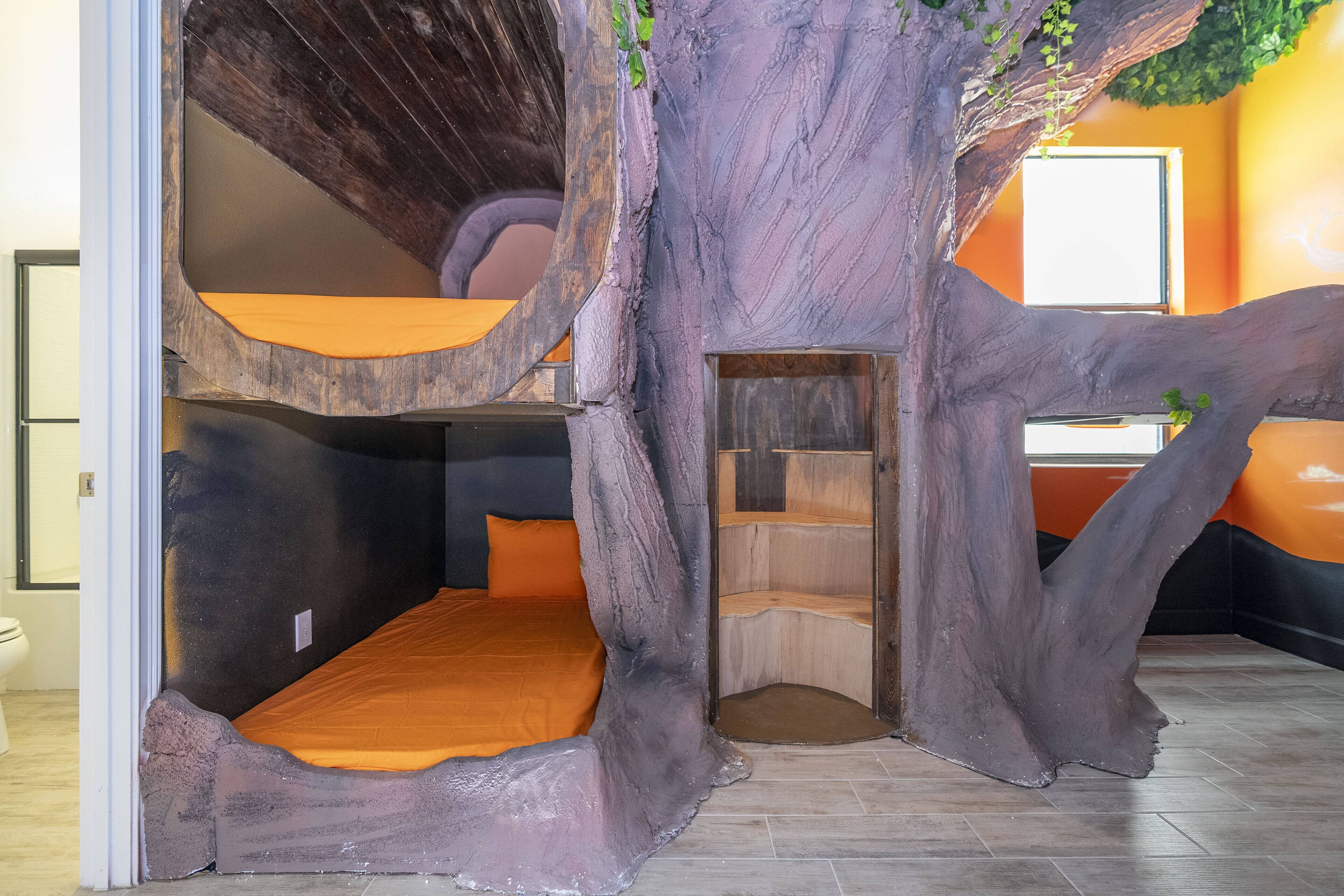 A tree-themed room with bunk beds, a small enclosed seating area, and a window.