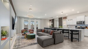 Una sala de estar moderna con un sofá modular, una mesa de centro y un televisor. La habitación tiene un ventanal y vistas al exterior.