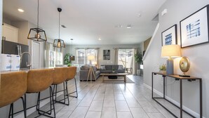 A modern kitchen with bar stools, a dining table, and a living area with a sofa and coffee table. - Last Minute Disney Getaway! Private Pool & Themed Bedrooms. Book Now! #127919 (Orlando)