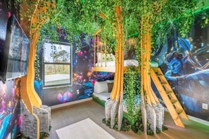 Relax in a serene space with a bed against a forest mural, a wooden ladder leading to a raised platform, and a large window for a peaceful view.