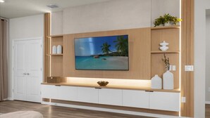 Una sala de estar moderna con un televisor de pantalla plana grande montado en una pared de madera, un mueble blanco debajo y un estante pequeño con objetos decorativos.
