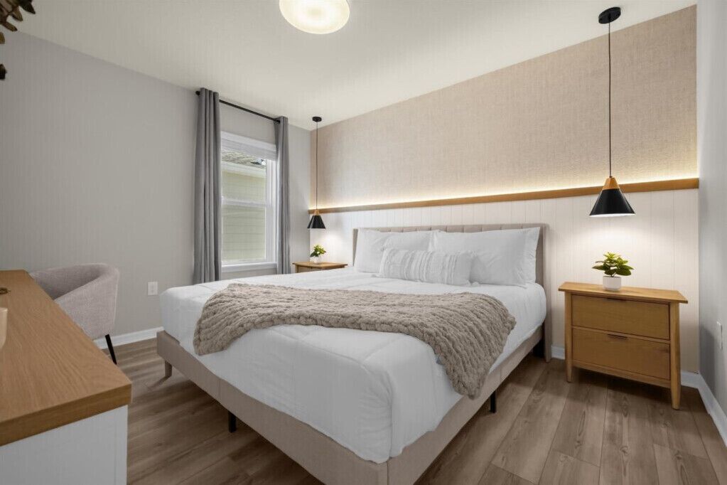 A modern bedroom with a large bed, bedside tables, a desk, and a window with curtains.