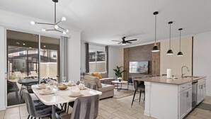 A modern kitchen with a central island, dining area with chairs, and a large window overlooking a balcony.