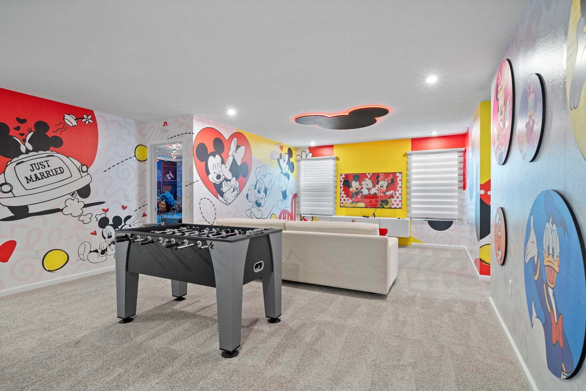 A room with a foosball table, colorful wall art, and a white sofa.