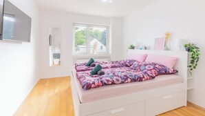 Un dormitorio con cama, ventana, televisor y planta.