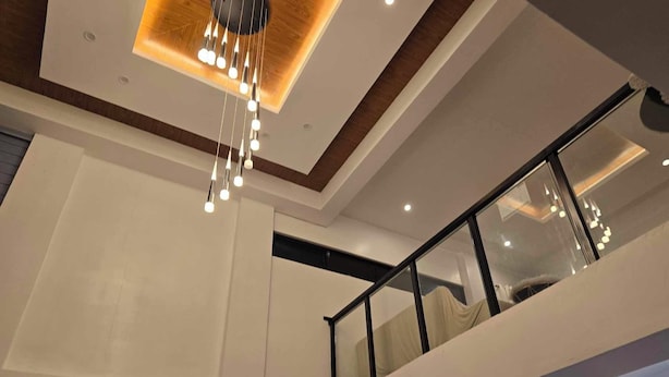Un intérieur moderne à plusieurs niveaux, comprenant un balcon avec des garde-corps en verre et un luminaire suspendu.