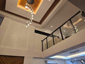 A modern interior with a multi-level design, including a balcony with glass railings and a hanging light fixture. - Exclusive Subdivision, Located near the Highway, Malls, school, Hospital. (Bacolod)