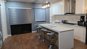Une cuisine moderne dotée d’un îlot central, de tabourets de bar, d’une hotte en acier inoxydable et d’un four à micro-ondes.