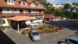 Ein zweistöckiges Gebäude mit überdachter Parkmöglichkeit, einem weißen Auto unter der Überdachung und einem kleinen Garten mit bunten Pflanzen.