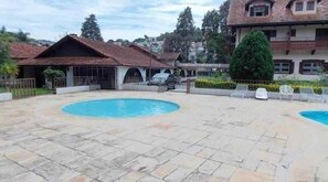 A courtyard with a swimming pool, a covered seating area, and a two-story building with a balcony. - HOTEL FLORESTA (Poços de Caldas)
