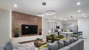 A modern living room with a grey sectional sofa, a round coffee table, and a flat-screen TV mounted on a wooden wall. - Last Minute Disney! Private Pool, Game Room & Themed Bedrooms. Book Now! #120787 (Orlando)