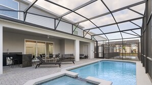 A swimming pool with a glass enclosure, lounge chairs, and a patio area with a grill and seating. - Last Minute Disney! Private Pool, Game Room & Themed Bedrooms. Book Now! #120787 (Orlando)