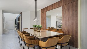 A modern dining area with a long table, multiple chairs, and a large mirror on one wall. - Last Minute Disney! Private Pool, Game Room & Themed Bedrooms. Book Now! #120787 (Orlando)
