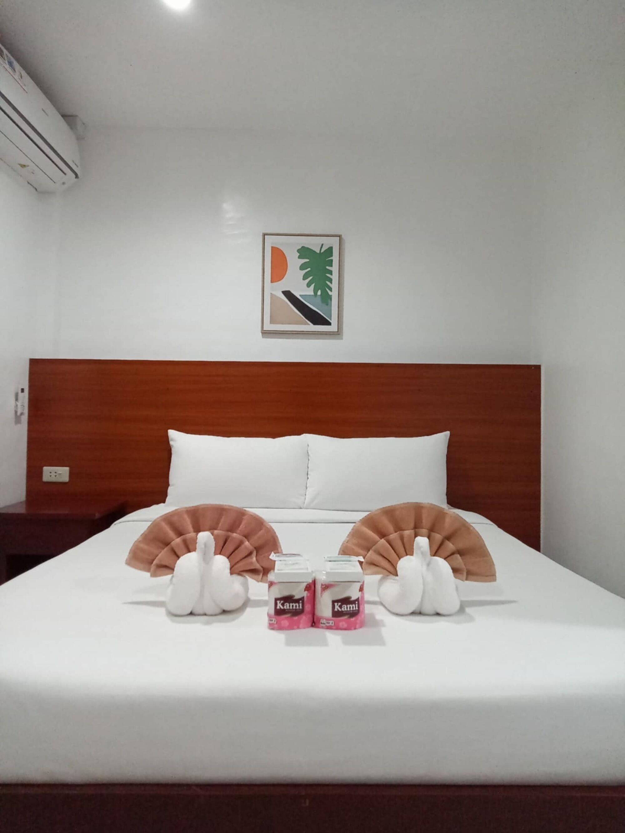 Quarto de hotel com cabeceira de madeira, roupa de cama branca, um quadro na parede e duas mesas de cabeceira.