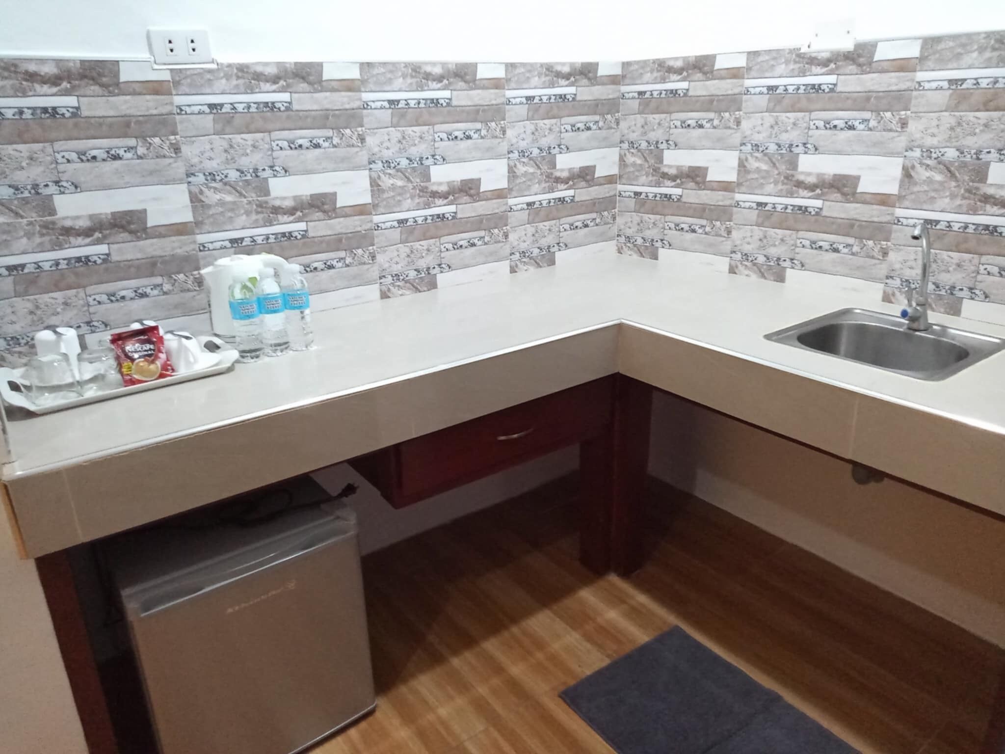 Eine kompakte Küche mit gefliestem Spritzschutz, Spüle, kleinem Kühlschrank und einer Arbeitsplatte mit diversen Gegenständen.