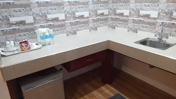 Eine kompakte Küche mit gefliestem Spritzschutz, Spüle, kleinem Kühlschrank und einer Arbeitsplatte mit diversen Gegenständen.